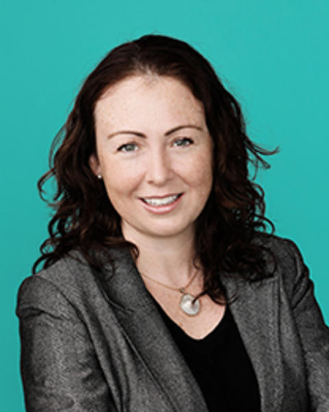 Alicia Grace Harley headshot - smiling with arms folded and teal background